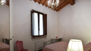 A bedroom with a bed, a chair, a window with curtains, a radiator, and a lamp. - Il Borgo di Badia-La Camelia (Buti)