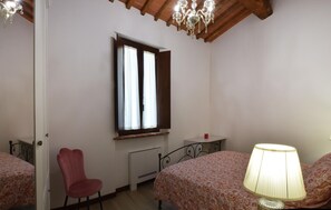 Ein Schlafzimmer mit Bett, Sessel, einem Fenster mit Vorhängen, Heizkörper und Lampe.