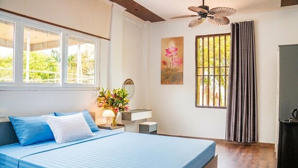 A bedroom with a bed, a desk, a chair, a window with curtains, and a ceiling fan. - Favos Bich Dong (Ninh Binh)