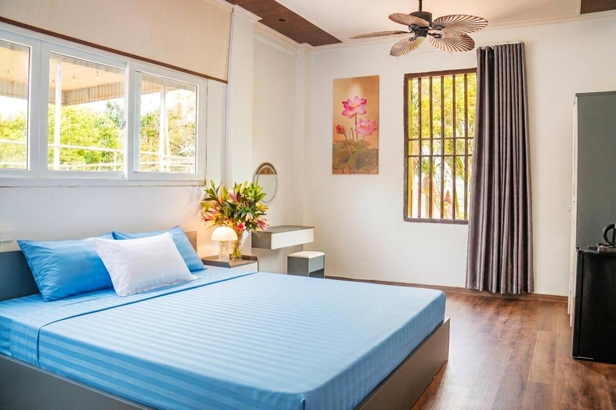 Quarto com cama, escrivaninha, cadeira, janela e ventilador de teto.