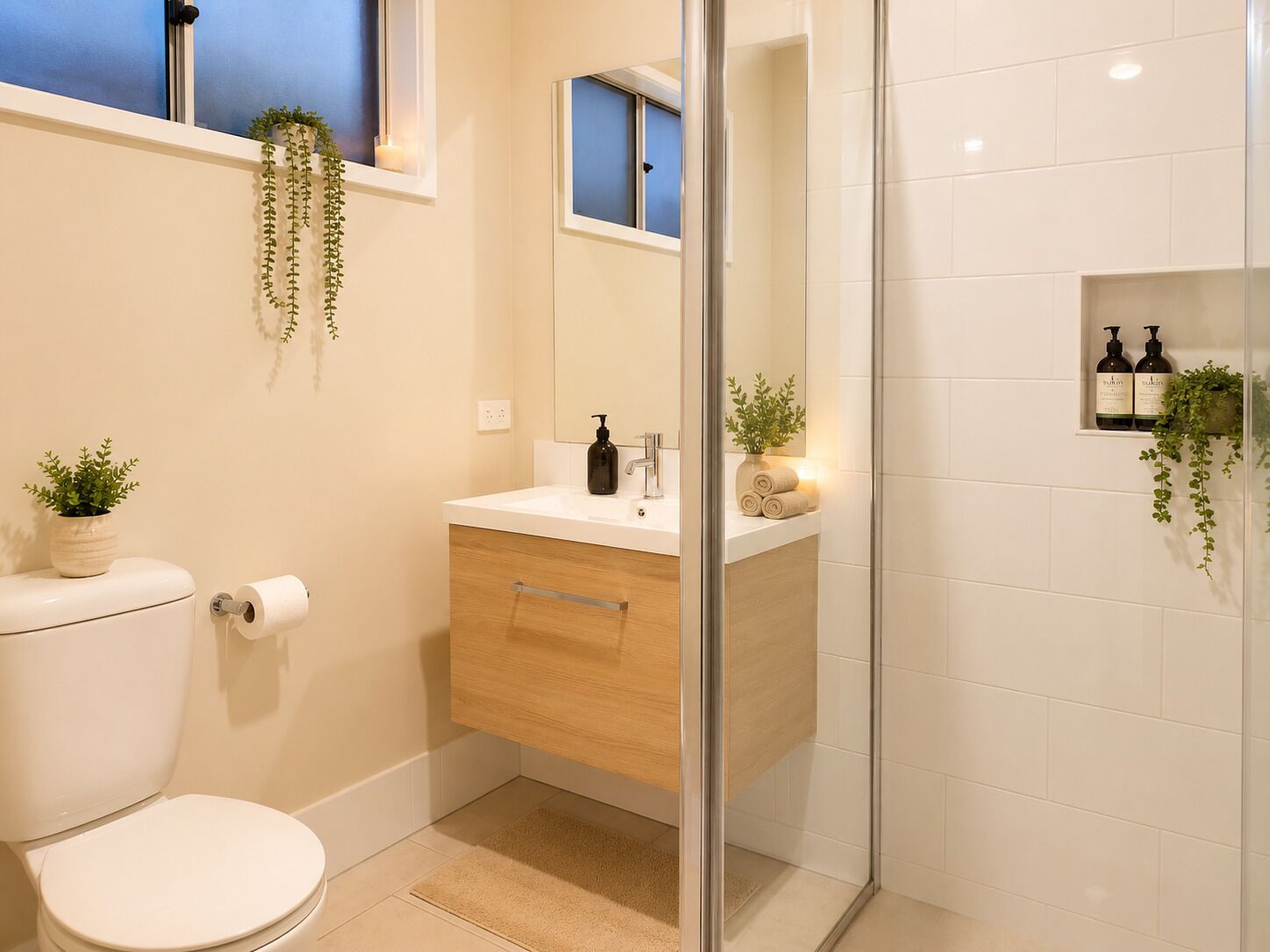 Une salle de bain comprenant des toilettes, un lavabo avec un miroir, un espace douche et des plantes en pot.