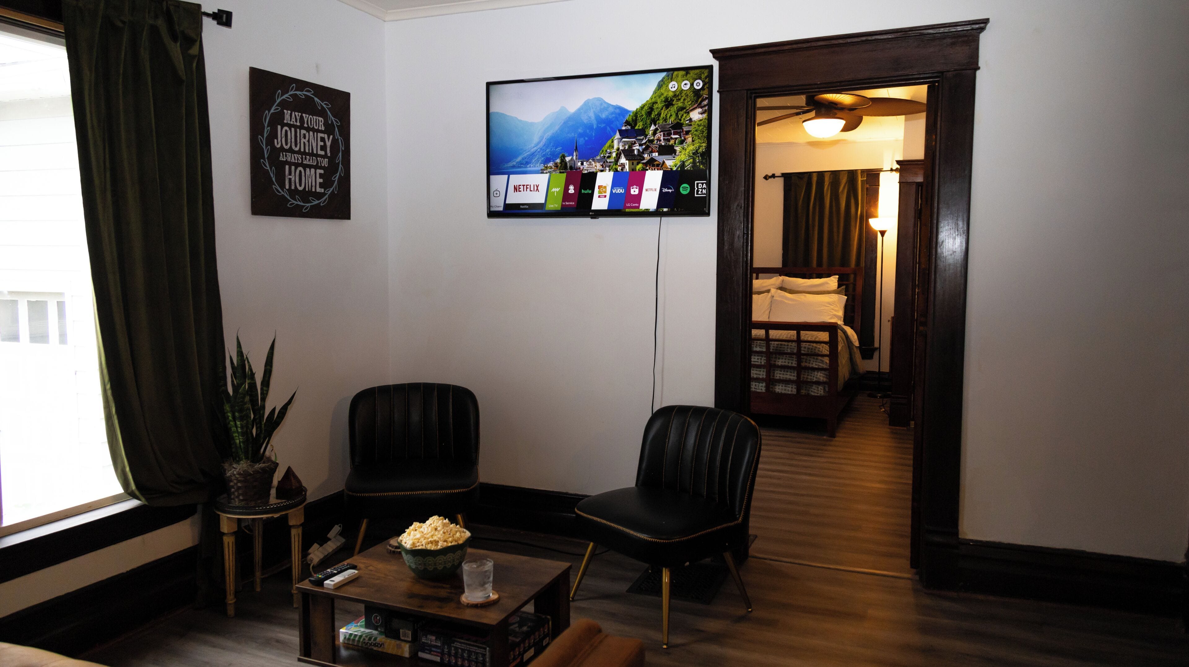 Une chambre d’hôtel équipée d’une télévision permettant d’accéder à des services de diffusion en continu, d’un lit, d’un coin salon avec des fauteuils, d’une table basse avec un bol de pop-corn et d’une plante en pot.