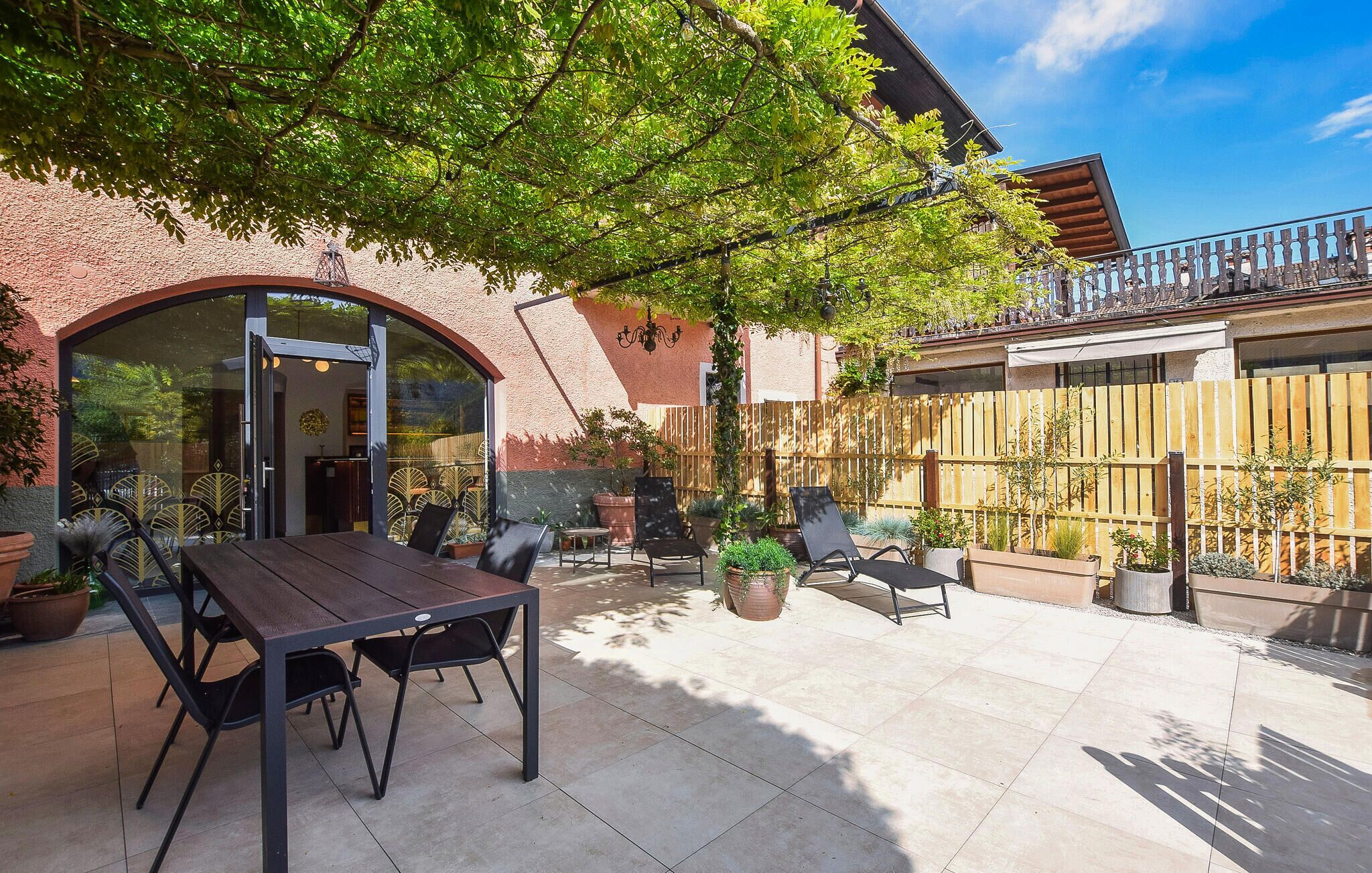 A patio with a table and chairs, surrounded by potted plants and a wooden fence.