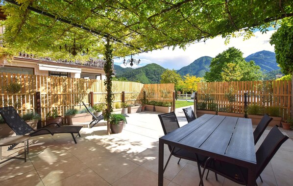 Eine Terrasse im Freien mit Tisch und Stühlen, umgeben von Holzzäunen und Kübelpflanzen.