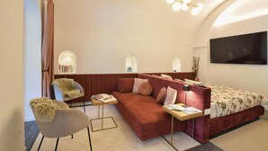 Een moderne hotelkamer met een bank, fauteuil, nachtkastje en een televisie.
