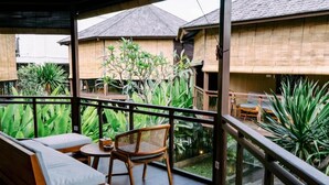 A covered outdoor seating area with a view of traditional wooden buildings and lush greenery. - Samada Work Life Canggu (Tumbak Bayuh)