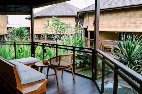 A covered balcony with wooden furniture, a view of traditional buildings, and lush greenery.. Samada Work Life Canggu