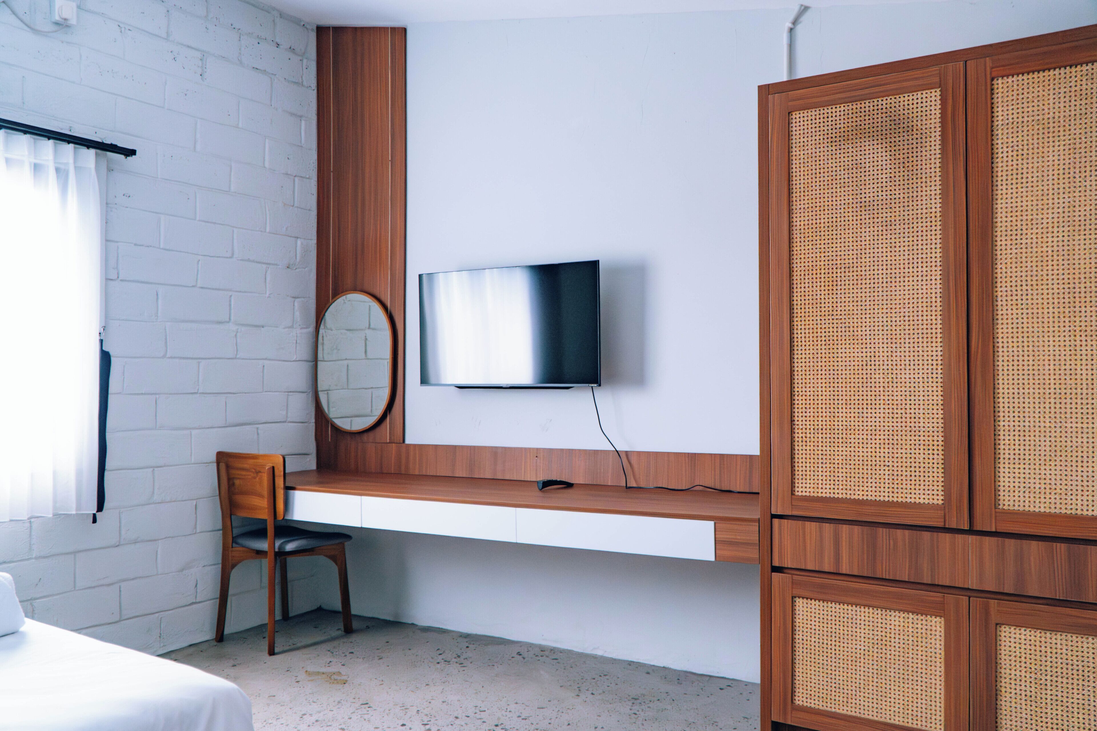 A room with a bed, a desk with a chair, a television mounted on the wall, and a wardrobe.