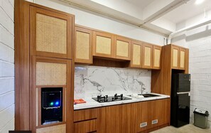 A kitchen with wooden cabinets, a marble countertop, a black refrigerator, and a built-in microwave. - Samada Work Life Canggu (Tumbak Bayuh)