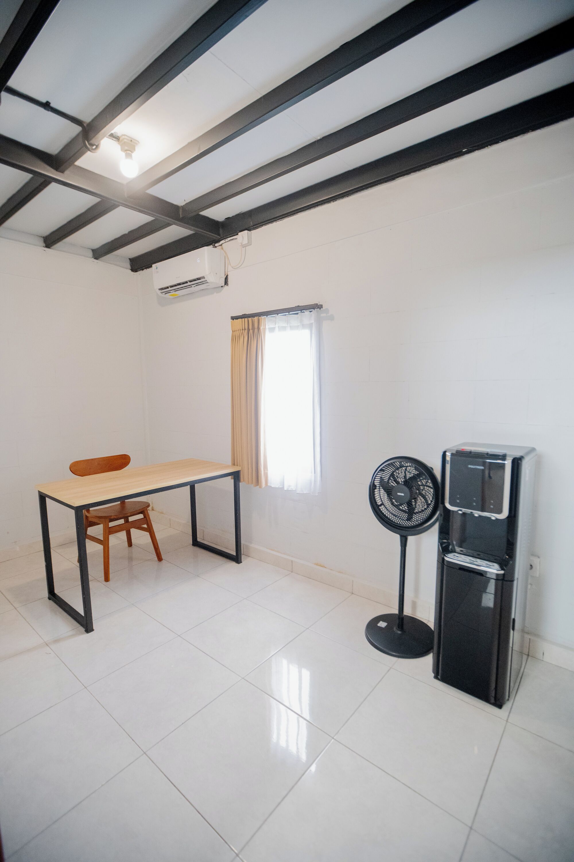 Une pièce comprenant une table, une chaise, un ventilateur sur pied et un distributeur d’eau.