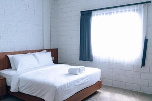 A single bed with white bedding, a wooden headboard, a nightstand, and a window with a blue curtain.