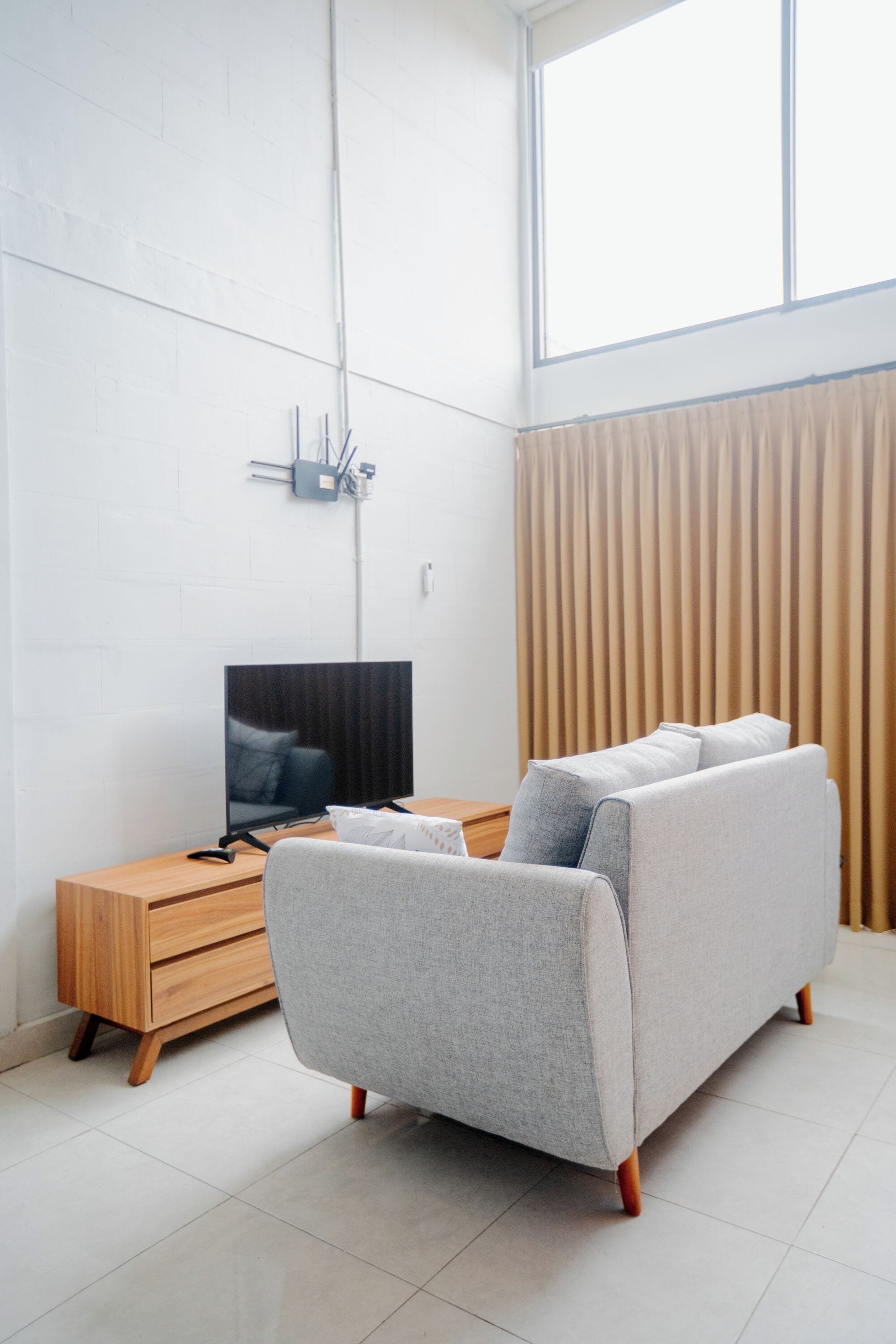 Una sala moderna con sofá, televisor, mesita de madera y una ventana con cortinas.