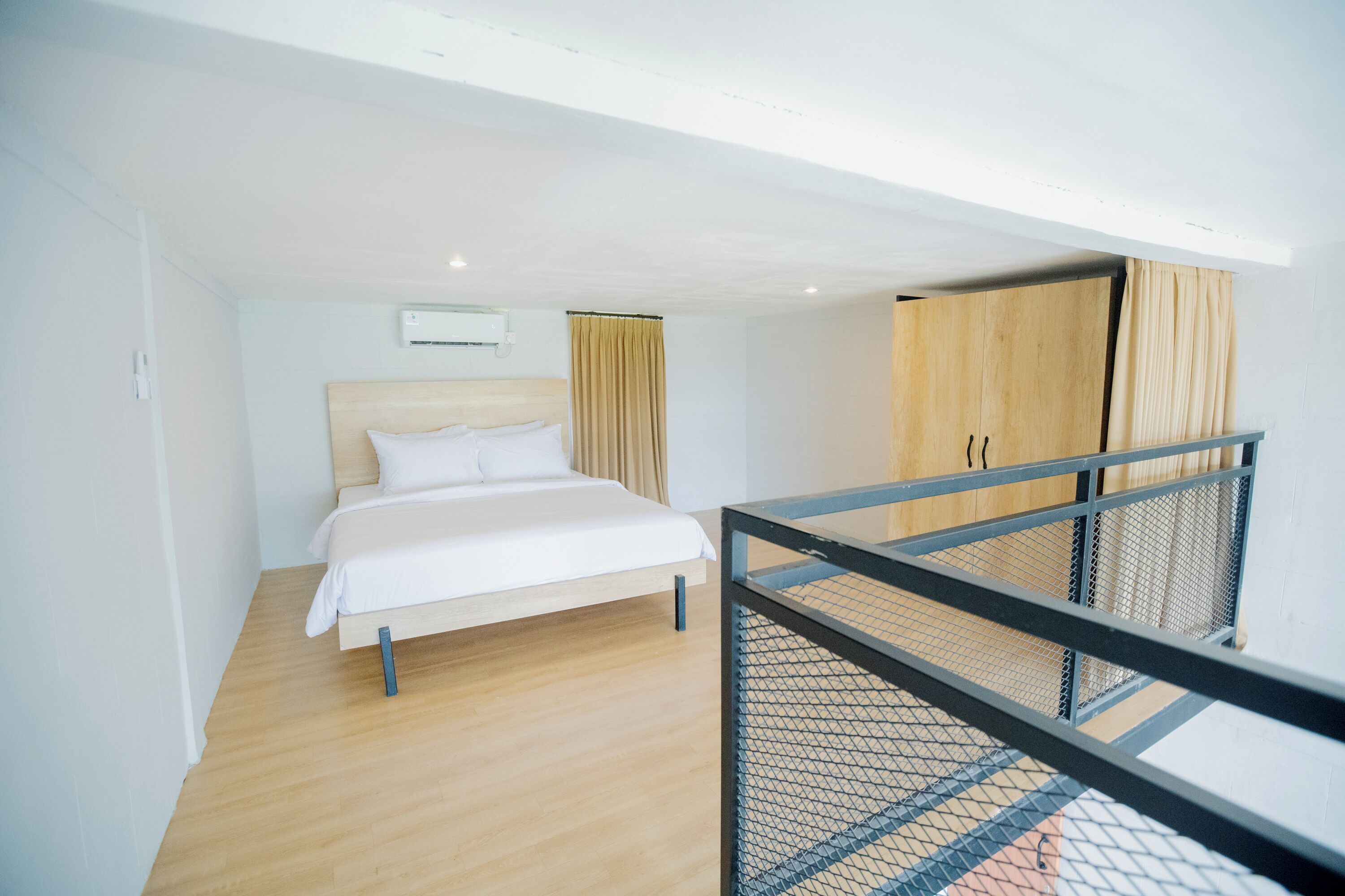 A modern hotel room with a bed, a wardrobe, and a balcony with a railing.