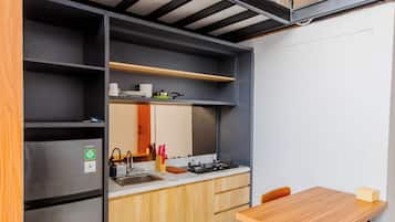 Una cocina compacta con refrigerador integrado, un lavamanos y una mesa de comedor de madera.
