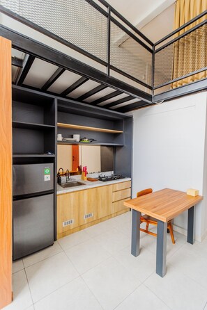 A compact kitchen with a built-in refrigerator, a sink, and a wooden dining table. - Samada Work Life Canggu (Tumbak Bayuh)