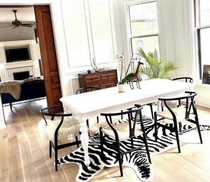 Ein Essbereich mit einem weißen Tisch, schwarzen Stühlen, einem zebra-gemusterten Teppich und einer Pflanze auf dem Tisch.