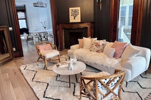Ein Wohnzimmer mit einem weißen Sofa, zwei Sesseln, einem Couchtisch, einem Kamin und einem Essbereich im Hintergrund.