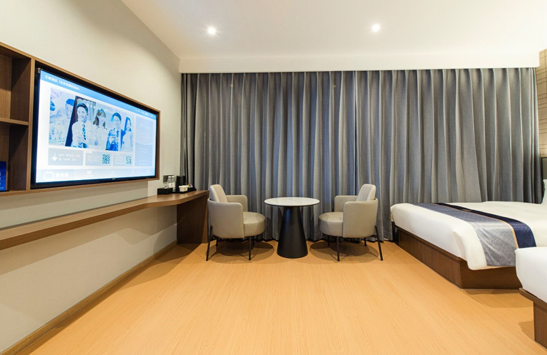 A hotel room with a bed, a TV on the wall, a small table, two chairs, and a curtain.