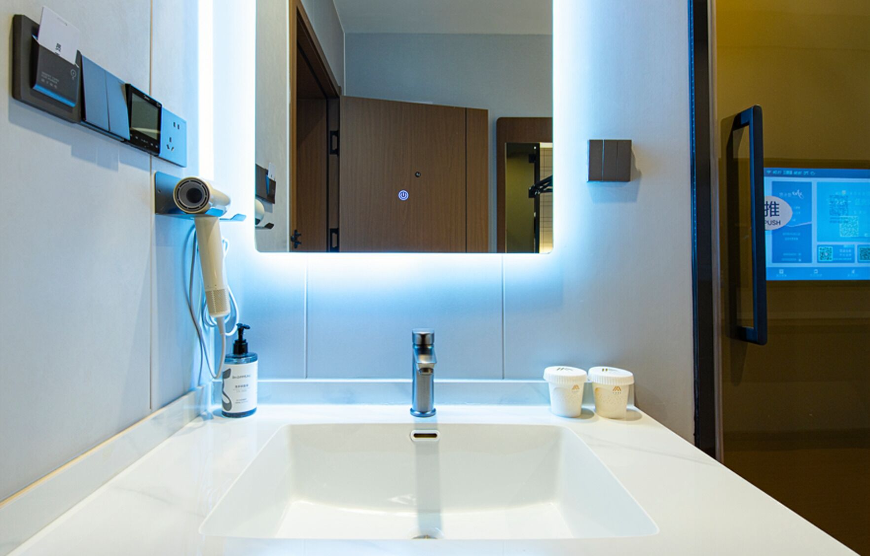 Un baño moderno con un espejo grande, un lavabo, un secador de pelo y dos tazas en la encimera.