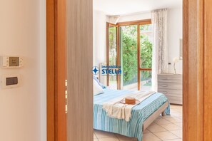 Een slaapkamer met een bed, een ladekast, een raam met gordijnen en uitzicht op groen.
