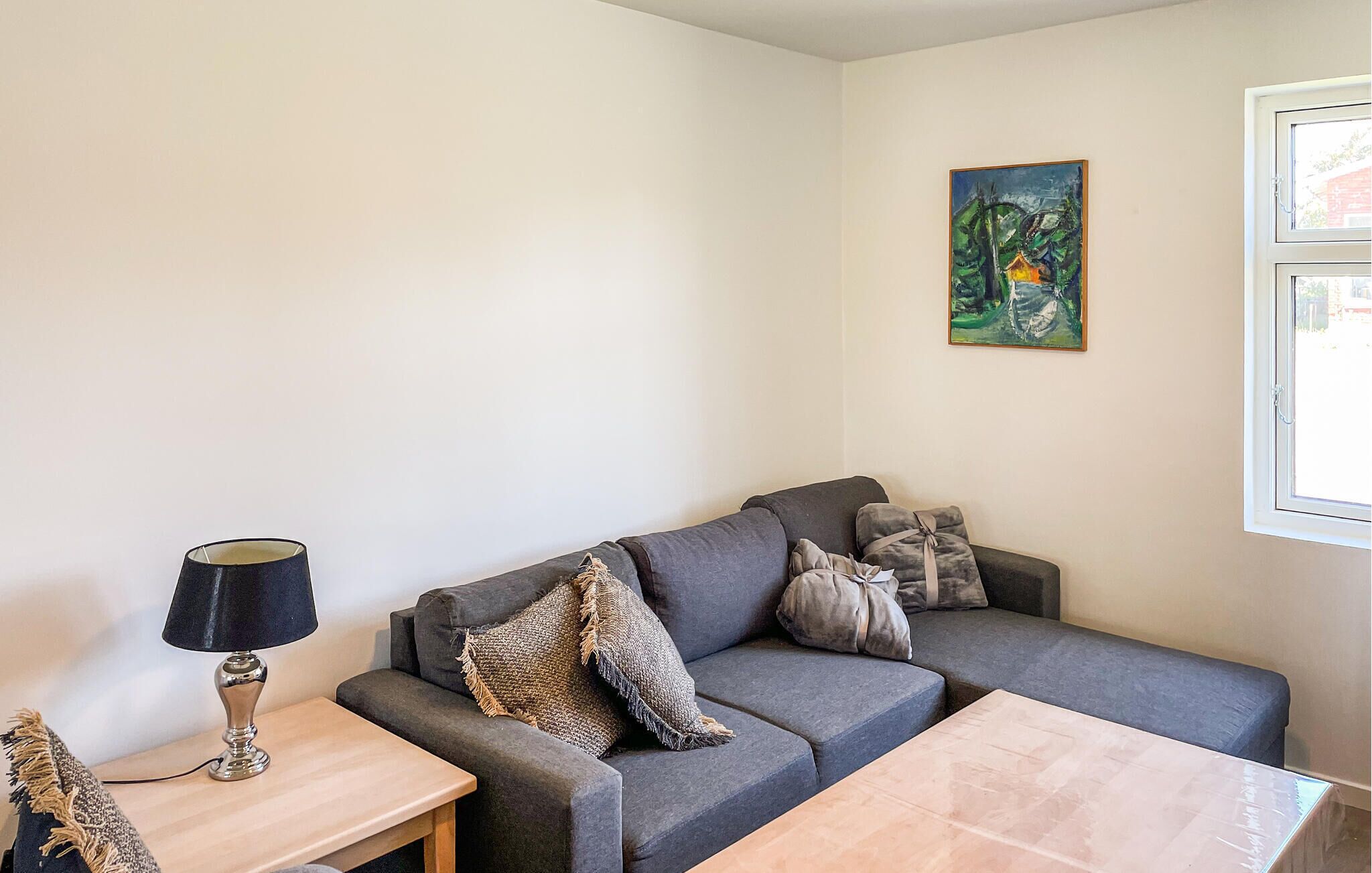 A living room with a grey sofa, a small wooden table, a lamp, and a painting on the wall.
