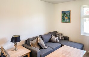 Una sala de estar con un sofá gris, una mesita de madera, una lámpara y un cuadro en la pared.