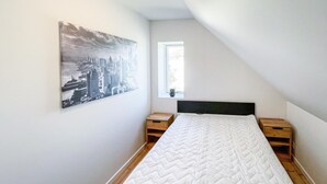 Ein Schlafzimmer mit Bett, Nachttisch, Fenster und einem Stadtbild an der Wand.