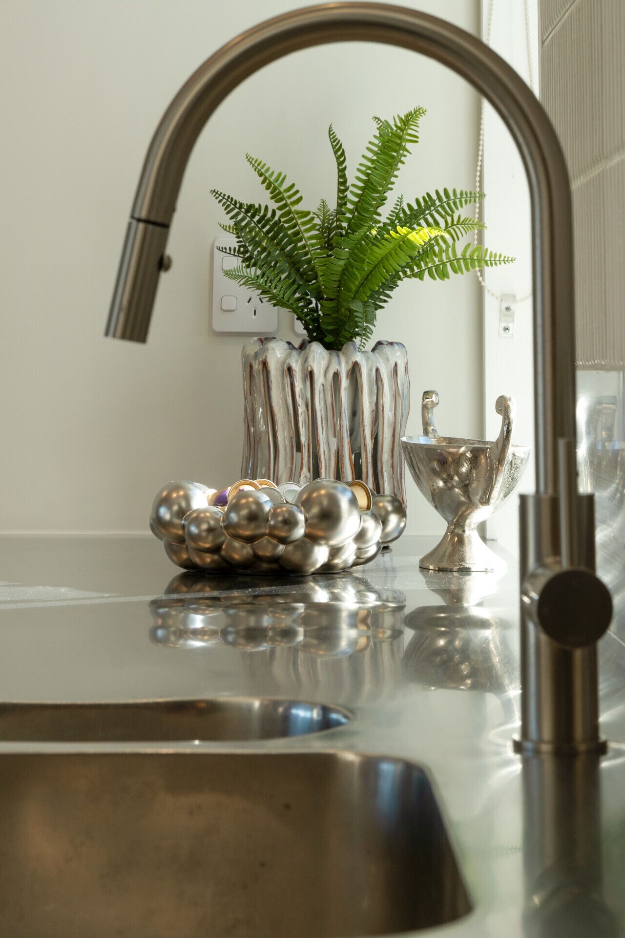 A kitchen sink with a modern faucet, a decorative plant in a vase, and a silver trophy on the countertop.