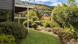 Ein modernes Haus mit einem Glasbalkon mit Blick auf einen gepflegten Garten und eine hügelige Landschaft im Hintergrund.