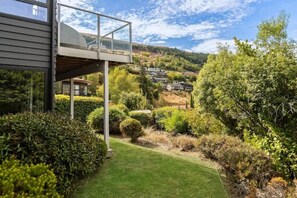 Une maison moderne dotée d’un balcon en verre qui offre une vue sur un jardin bien entretenu et, au loin, sur un paysage vallonné.