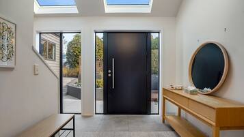 A modern interior with skylights, a black door, a wooden bench, and a round mirror on a wooden console.