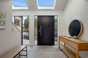 Ein modernes Interieur mit Oberlichtern, einer schwarzen Tür, einer Holzbank und einem runden Spiegel auf einer Holztruhe.
