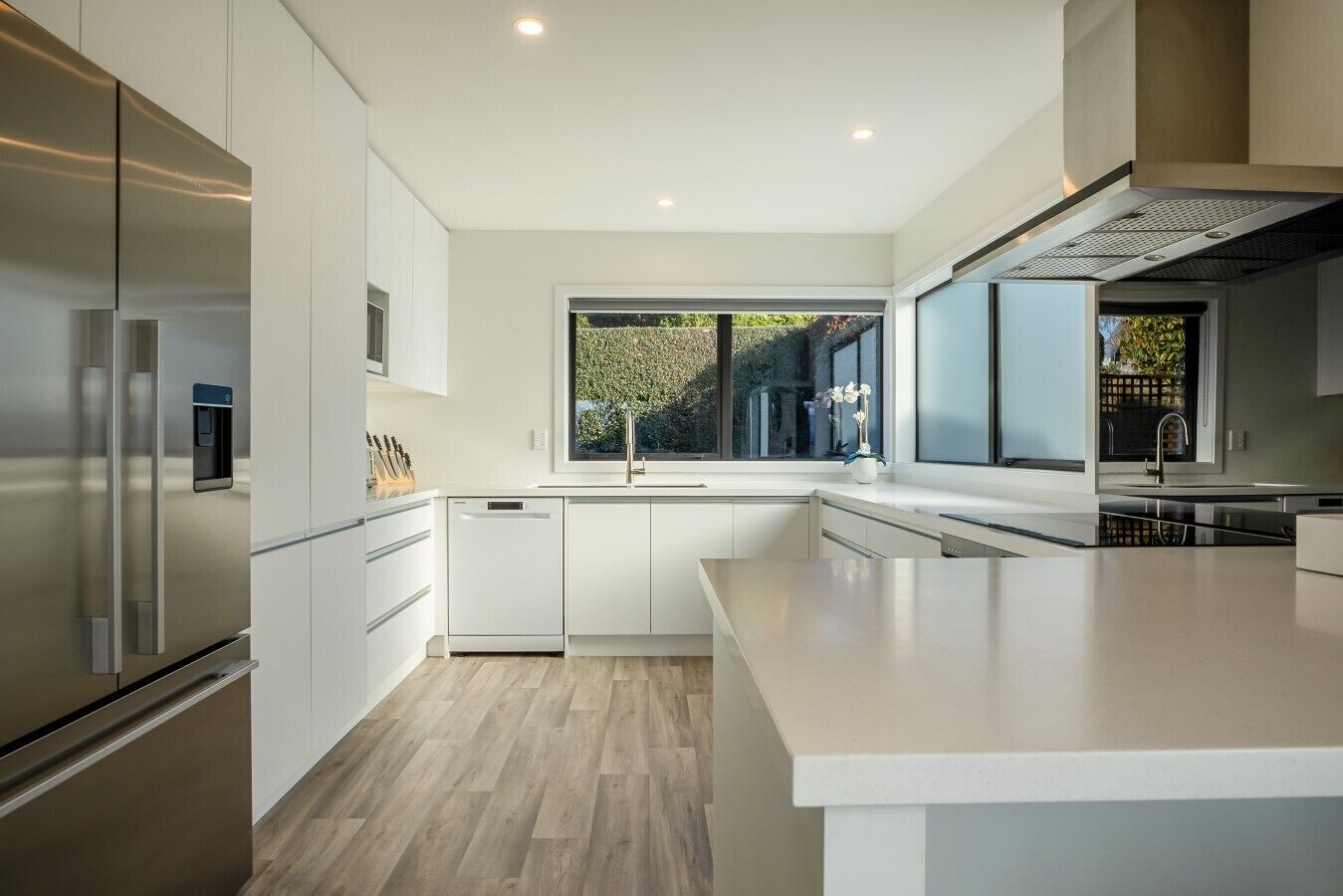 A modern kitchen with white cabinetry, stainless steel appliances, and a large window.