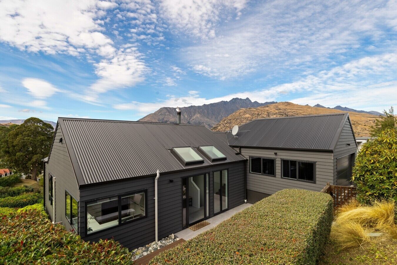 A modern two-story house with a sloped roof, large windows, and a view of mountains.