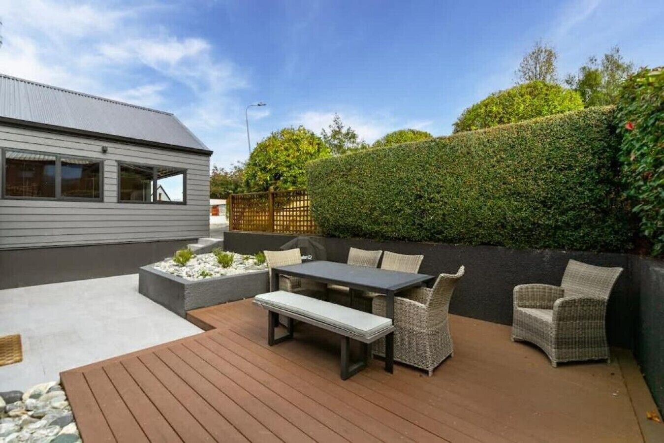 Une terrasse avec une table et des chaises, une plateforme en bois et une haie.