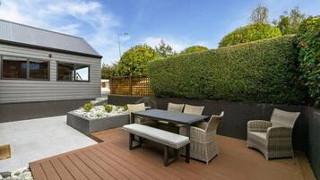 Une terrasse avec une table et des chaises, une plateforme en bois et une haie.