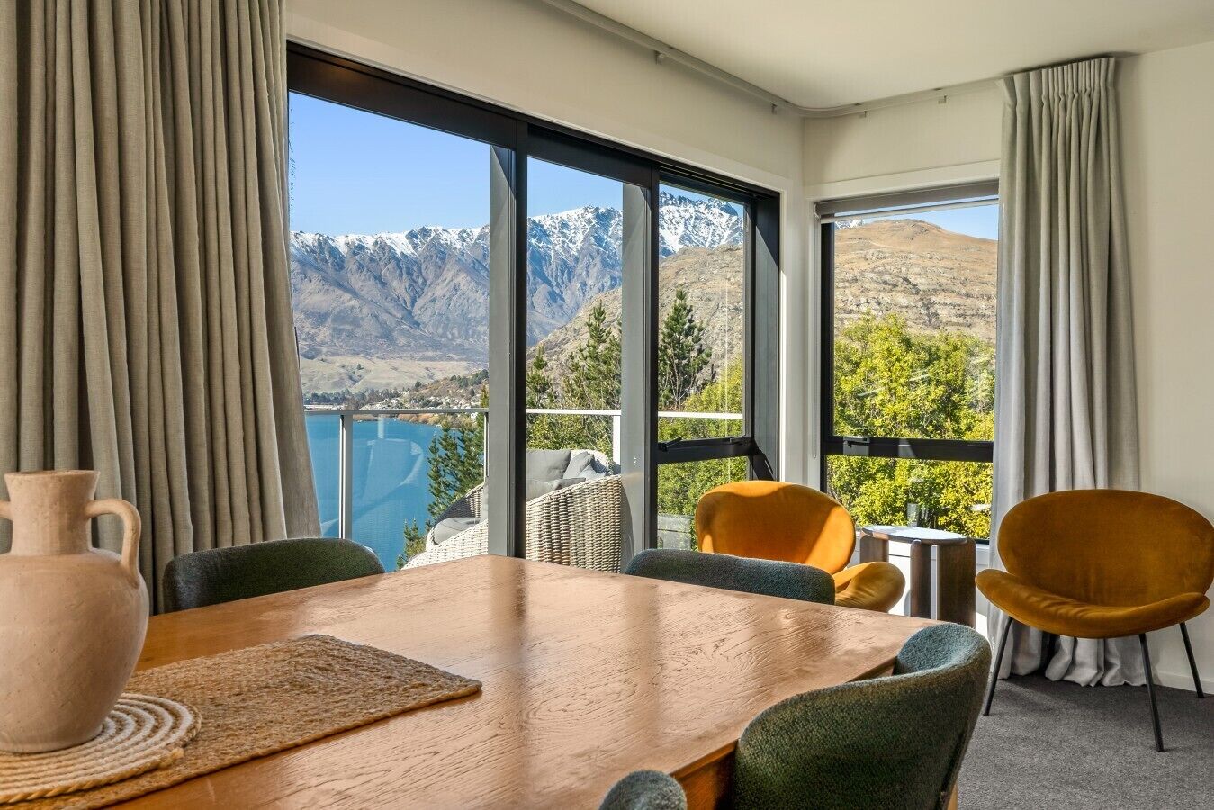 Ein Zimmer mit Holztisch, Stühlen und Blick auf Berge und einen See.