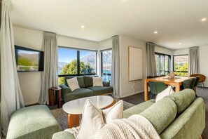 A modern living room with a sofa, a coffee table, and a dining area with chairs and a table. - The Gold Rise-| Two Living Areas-· Big Outdoors (Queenstown)