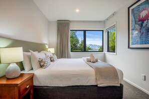 Une chambre à coucher avec un lit, une table de chevet, une lampe et une fenêtre donnant sur un paysage verdoyant et montagneux.