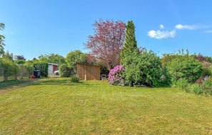 A grassy backyard with a wooden shed, a red building, and various trees and shrubs.