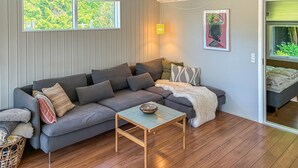 A modern living room with a grey sofa, a wooden coffee table, and a view of greenery through the windows. - 2 bedroom stunning home in Vordingborg (Vordingborg)