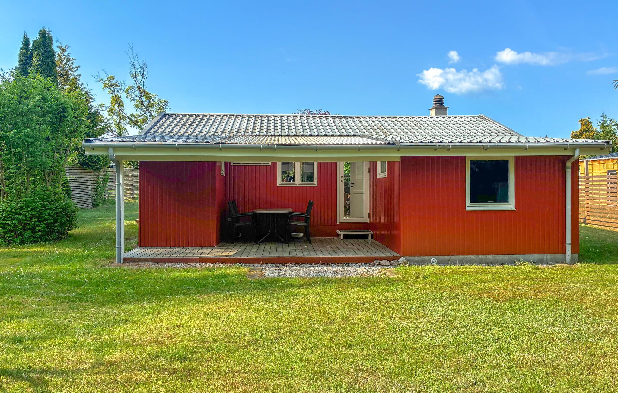 A red single-story house with a tiled roof, a small porch, and a table with chairs.