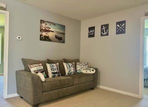 A living room with a grey couch, a painting of a lake, and three wall signs with nautical themes. - D's Creekside NorthCarolinaHome Apartment A (Burlington)