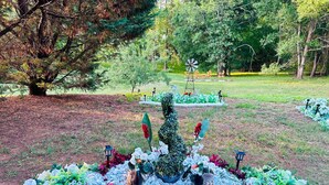 Ein Garten mit einer zentralen Skulptur, umgeben von verschiedenen Pflanzen und Blumen.