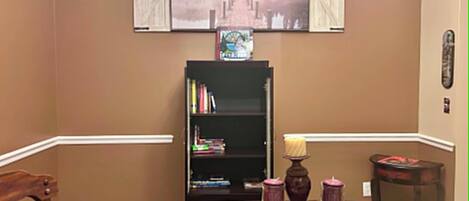 A dining area with a table set for two, a bookshelf, and a mounted television displaying a scenic image.
