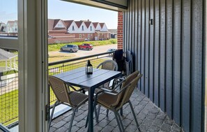 A balcony with a table and chairs, a view of houses and parked cars, and a metal railing. - Amazing apartment in Fanø with WiFi (Fanø)