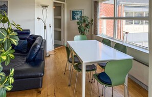 A room with a black leather sofa, a white table, green chairs, a potted plant, and a window with a view of a brick building. - Amazing apartment in Fanø with WiFi (Fanø)