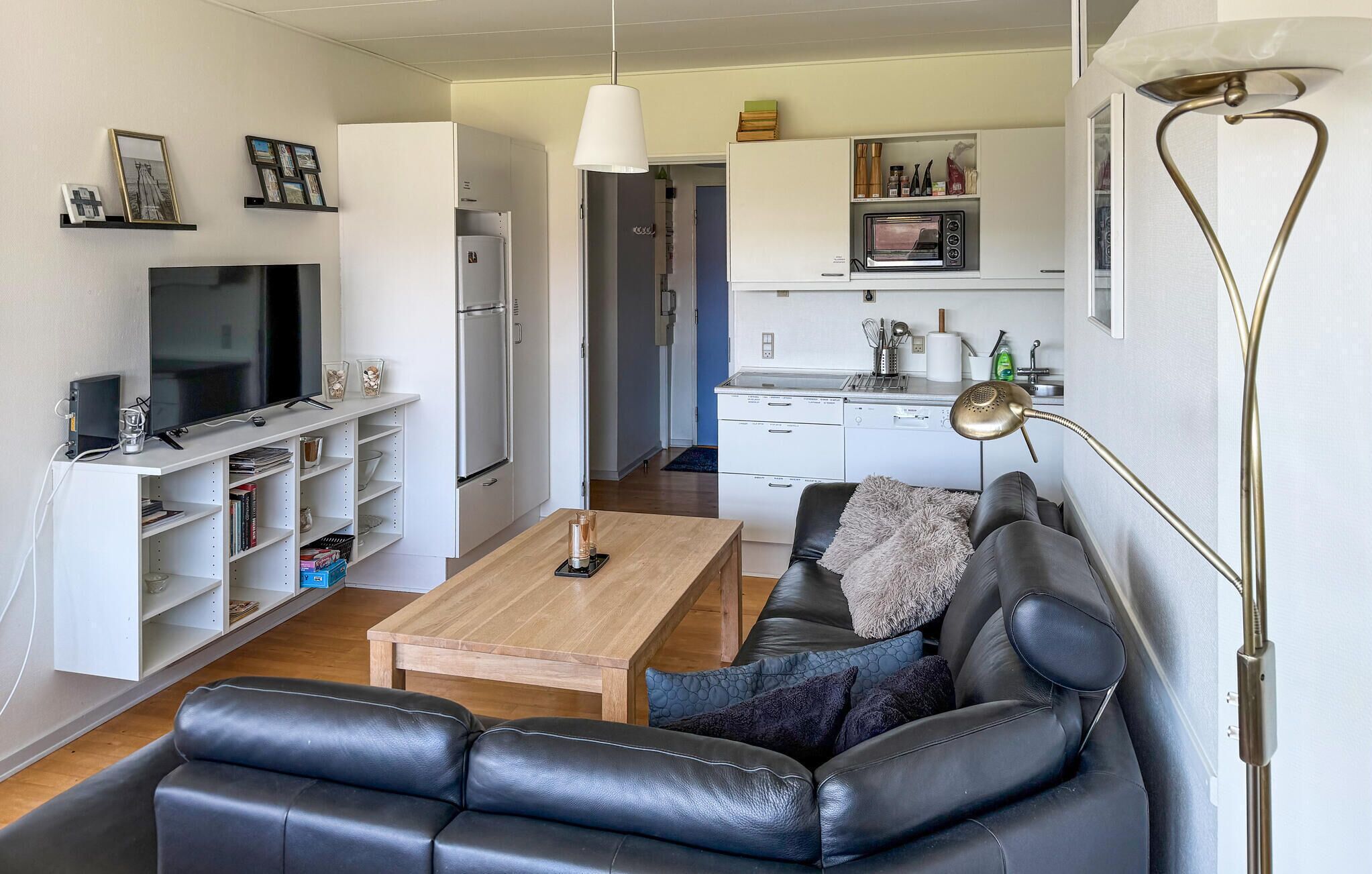 Un salon avec un canapé en cuir noir, une table basse en bois, un téléviseur et un meuble blanc avec des étagères.