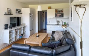 A living room with a black leather sofa, a wooden coffee table, a TV, and a white cabinet with shelves. - Amazing apartment in Fanø with WiFi (Fanø)
