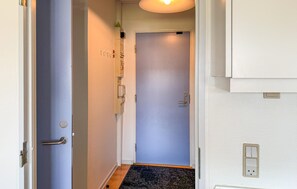 A narrow hallway with a blue door at the end, a light fixture above, and a doorbell on the wall. - Amazing apartment in Fanø with WiFi (Fanø)